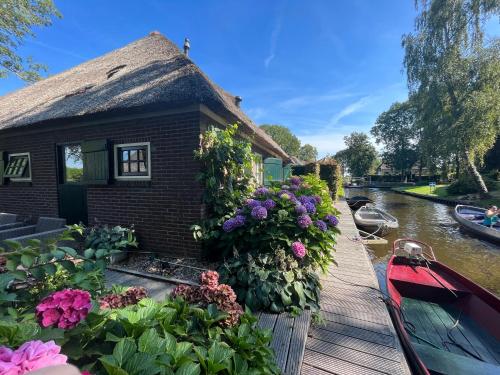 a house on a canal with flowers and a boat at Plompeblad Suite Giethoorn in Giethoorn