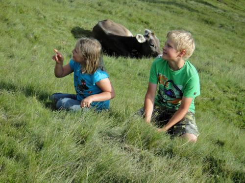 two children sitting in the grass near a cow at Berggasthof Schatzbergalm in Thierbach