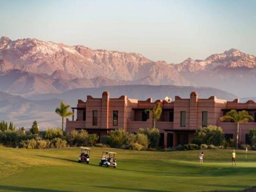 a building with two golf carts on a green with mountains in the background at Villa Marrakech piscine privée vue sur Golf&Atlas in Marrakech