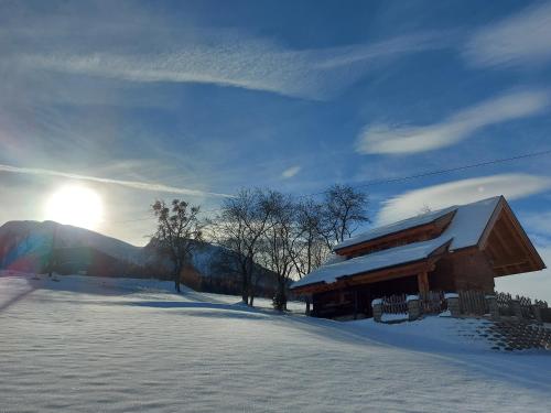 a log cabin in the snow with the sun behind it at Chalet Troadkasten Biohof Kreilgut in Walchegg