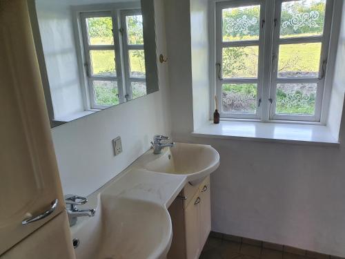 ein weißes Badezimmer mit zwei Waschbecken und zwei Fenstern in der Unterkunft Slotsgaardens feriegård. in Jels