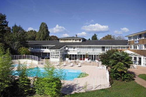 - un grand bâtiment avec une piscine en face dans l'établissement Hotel Belambra Le Normont, à Dourdan