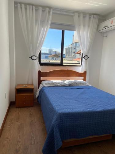 Un dormitorio con una cama azul y una ventana en Apto a 100m da praia -2 dorms 6 pessoas em Bombinhas, en Bombinhas
