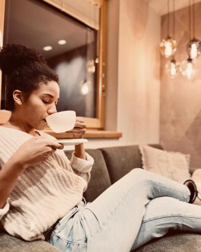 a woman sitting on a couch drinking a cup of coffee at Apart Harmonie in Kappl