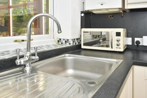 a kitchen counter with a sink and a microwave at Squirrel Cottage by YourStays in Stoke on Trent