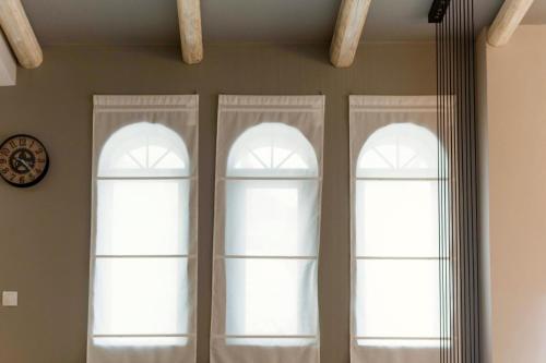 two windows with white curtains and a clock on a wall at Villa Murtal in Gerani