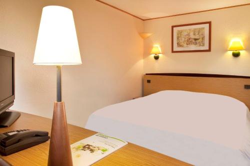 a hotel room with a bed and a desk with a lamp at Campanile Manosque in Manosque