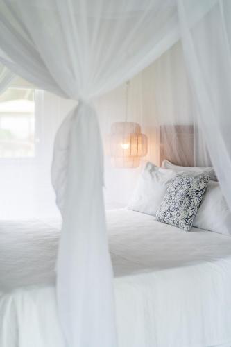 a white bedroom with a bed with pillows and a window at Orixás Residence in Morro de São Paulo