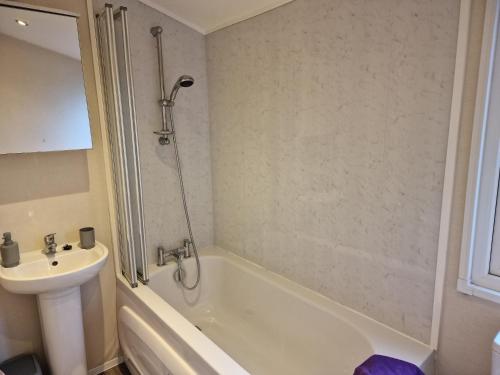 La salle de bains est pourvue d'une baignoire, d'un lavabo et d'une douche. dans l'établissement Bird Lake Pastures Holiday Caravan, à Northampton