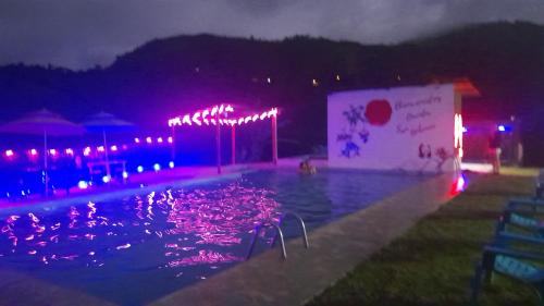 Hostería Quinta San Antonio في Nanegal: حمام سباحة في الليل مع أضواء أرجوانية
