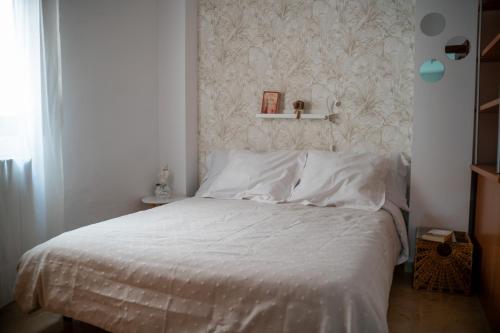a bedroom with a bed with white sheets and a wall at Bonito piso en San Ildefonso - Centro in Jaén