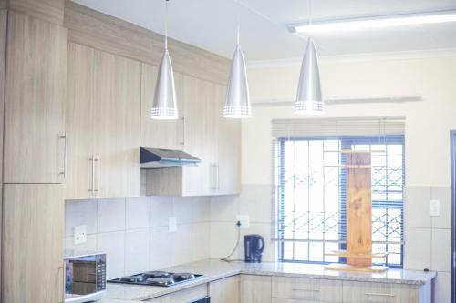 a kitchen with white cabinets and white pendant lights at Marelden estate in eMalahleni