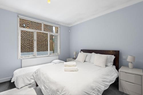 a white bedroom with a large bed and two windows at Londwell, Boutique Bliss Nestled in Knightsbridge by Harrods in London