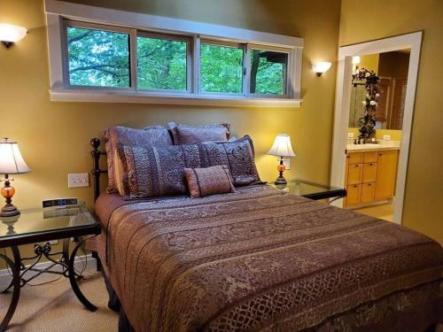 a bedroom with a large bed with two tables and two windows at Woodshores Retreat - cozy retreat, hot tub, Lk MI in Coloma