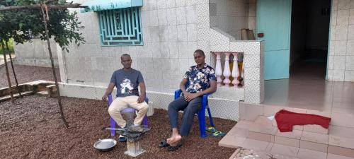 deux hommes assis sur des chaises devant un bâtiment dans l'établissement CHEZ TAHIROU Birfy, à Fatick