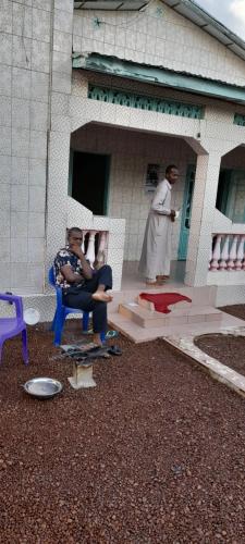 un homme assis sur une chaise devant un bâtiment dans l'établissement CHEZ TAHIROU Birfy, à Fatick