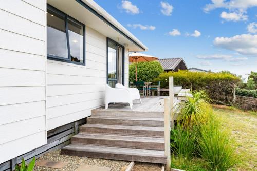 a house with a wooden staircase leading to a patio at The Summer Pad - Omaha Holiday Home in Warkworth