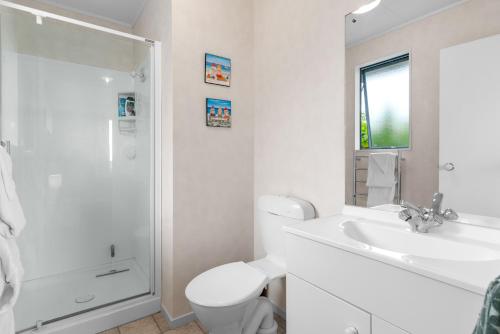 a white bathroom with a toilet and a sink at The Summer Pad - Omaha Holiday Home in Warkworth