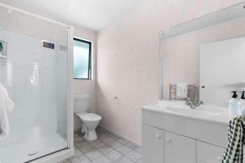 a white bathroom with a toilet and a sink at The Summer Pad - Omaha Holiday Home in Warkworth