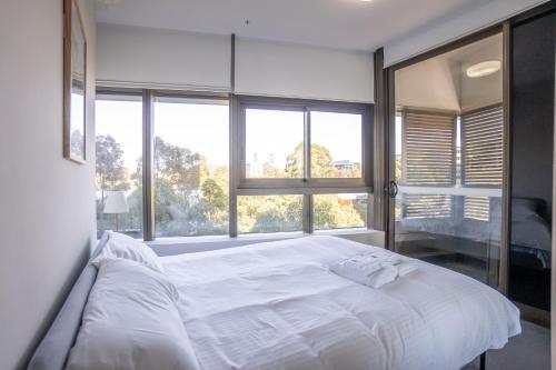 ein weißes Bett in einem Zimmer mit einem großen Fenster in der Unterkunft Olympic Park 2 Bedrooms Charm Family Friend Free Parking in Sydney
