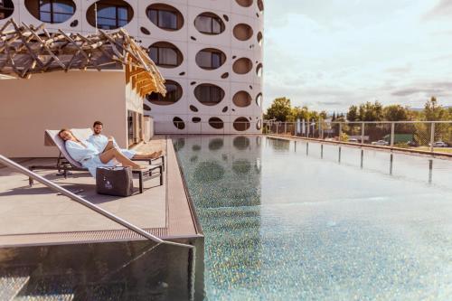 a man sitting in a chair next to a swimming pool at Das Seepark Wörthersee Resort in Klagenfurt