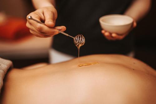 a woman drizzling honey onto a stomach with a spoon at Das Seepark Wörthersee Resort in Klagenfurt