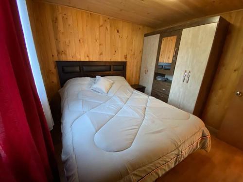 a bedroom with a white bed in a wooden room at Cabaña en sector residencial in Puerto Aisén