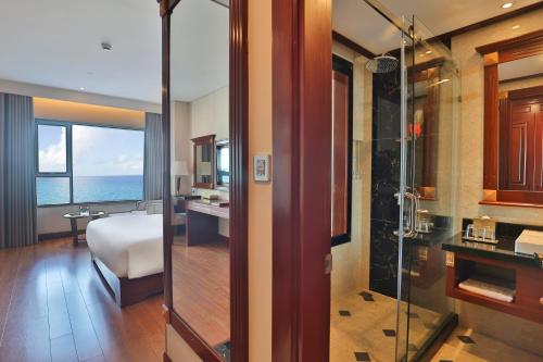 a bathroom with a shower and a bedroom with the ocean at DLG Hotel Danang in Da Nang