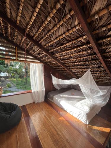 a bed in a thatched room with a window at Popochos Beach Eco Lodge in Nuquí