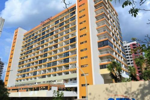 a tall yellow building with a palm tree in front of it at Garvey Hotel - Flat centro de Brasília in Brasilia