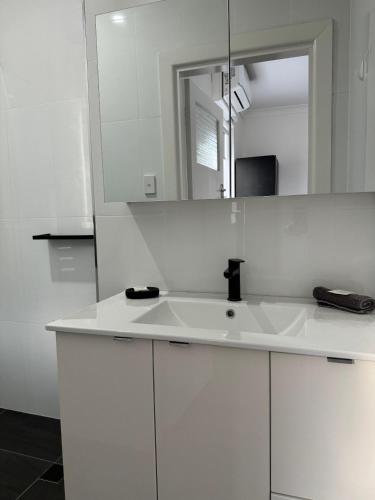 La salle de bains blanche est pourvue d'un lavabo et d'un miroir. dans l'établissement Away on Blende Studio Loft, à Broken Hill