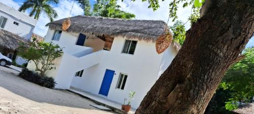 ein weißes Haus mit einem Strohdach und einem Baum in der Unterkunft Posada Mykonos in Bacalar