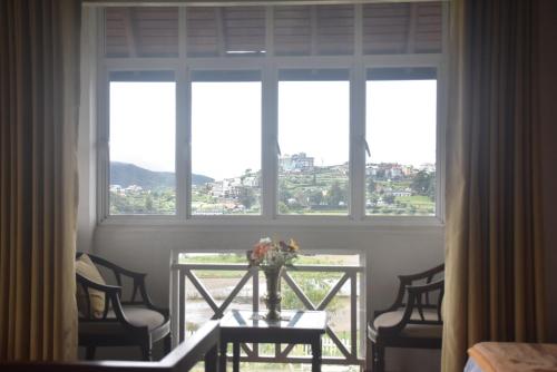 ヌワラエリヤにあるGregory's Bungalowのテーブルと椅子、大きな窓が備わる客室です。
