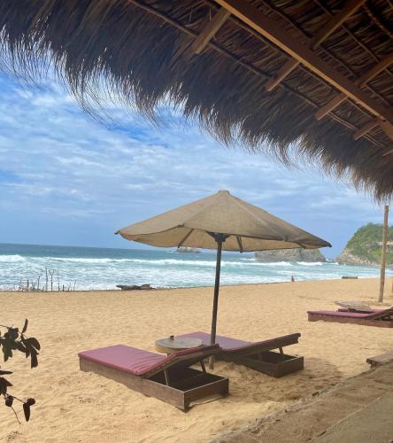 a beach with two lounge chairs and an umbrella at Posada Mexico in Zipolite