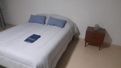 a white bed with blue pillows and a night stand at Mono ambiente a estrenar in Las Heras