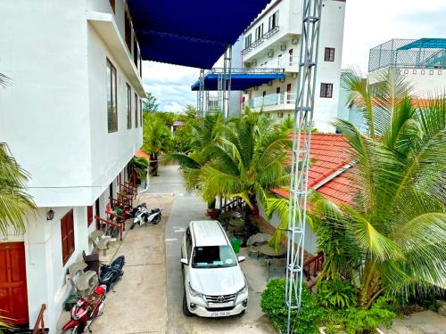 ein weißes Auto, das neben einem Gebäude mit Palmen parkt in der Unterkunft Sân Vườn Hotel Khánh Hòa in Ninh Hòa