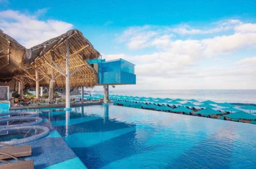 een zwembad met blauwe parasols en de oceaan bij Grant's Studio at Mantamar Tower in Puerto Vallarta