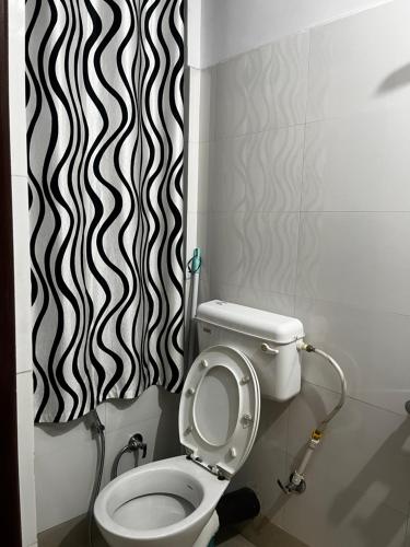 a bathroom with a toilet and a black and white shower curtain at EJ’s Frontyard- The Home Cafe & Stay in Kurseong