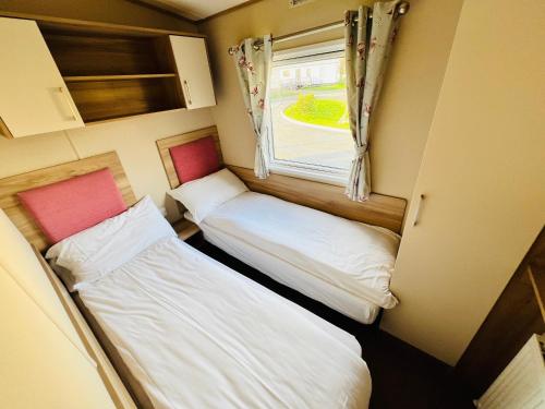 Duas camas num pequeno quarto com uma janela em 2 Bedroom Caravan CW111, Whitecliff Bay, Bembridge, Isle of Wight em Bembridge