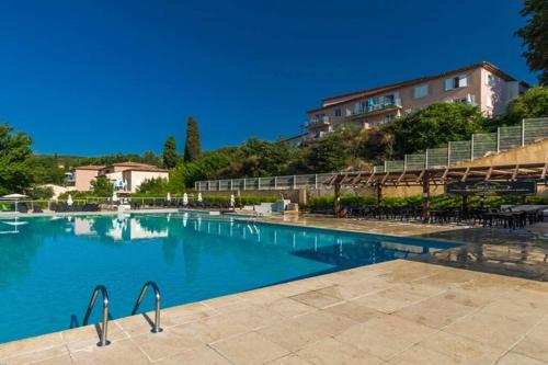 une grande piscine avec un bâtiment en arrière-plan dans l'établissement La Camiole Callian YourHostHelper, à Callian