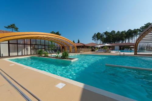 a large swimming pool with a bridge in front of a building at Les Cottages Du Lac in Parentis-en-Born