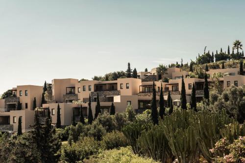a group of houses on a hill with trees at Phāea Blue - Small Luxury Hotels of the World in Elounda