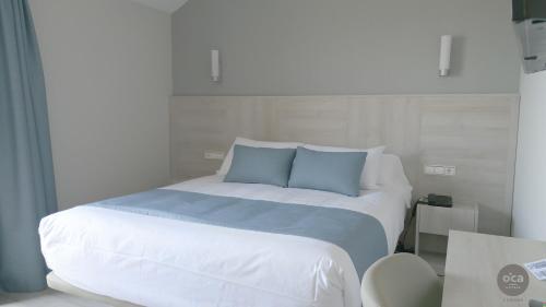 a white bed with blue pillows in a room at Hotel Oca Vermar in Aios