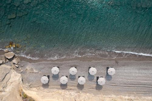 a group of umbrellas standing on the beach at KOIA All - Suite Well Being Resort - Adults Only in Agios Fokas
