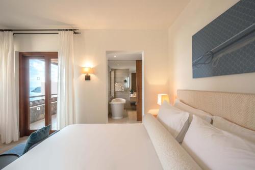 a bedroom with a large white bed and a bathroom at Phāea Blue - Small Luxury Hotels of the World in Elounda