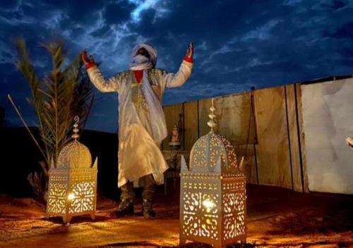 Un uomo in costume sta in piedi accanto alle lanterne di Fantastic Desert Luxury Camp a Merzouga