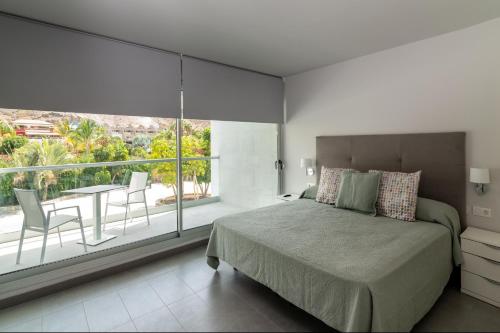 a bedroom with a bed and a balcony with a table and chairs at Apartamentos Cordial Mogán Paraíso in Puerto de Mogán