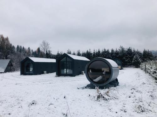 a round mirror sitting in the snow next to some green buildings at Chyża Zagroda in Jaworki