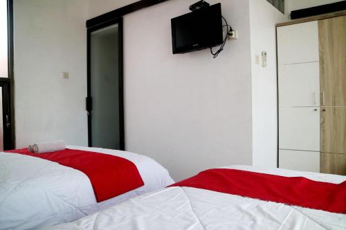 two beds in a room with a tv on the wall at The Homey Rooms and Tours in Yogyakarta