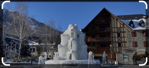une fontaine gelée devant un bâtiment enneigé dans l'établissement ST LARY SOULAN, à Saint-Lary-Soulan